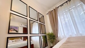 Een hotelkamer met een groot bed, een wandspiegel, een kamerplant en een raam met gordijnen.
