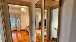 A hallway with wooden flooring, a large mirror, and a hanging light fixture.