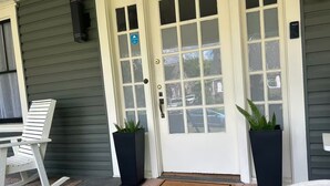 A front door with a 'WELCOME' mat, two potted plants, and a rocking chair on the porch.