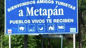 Segnaletica di benvenuto blu per Metapán con icone di una balena, una barca, una chiesa e una persona che nuota.