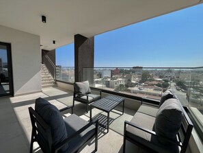 A balcony with a sofa, a table, and a chair. There is a staircase leading to an upper level. The balcony overlooks a cityscape. - 107 LIM - Stay Mouson View Apartment (Limassol)