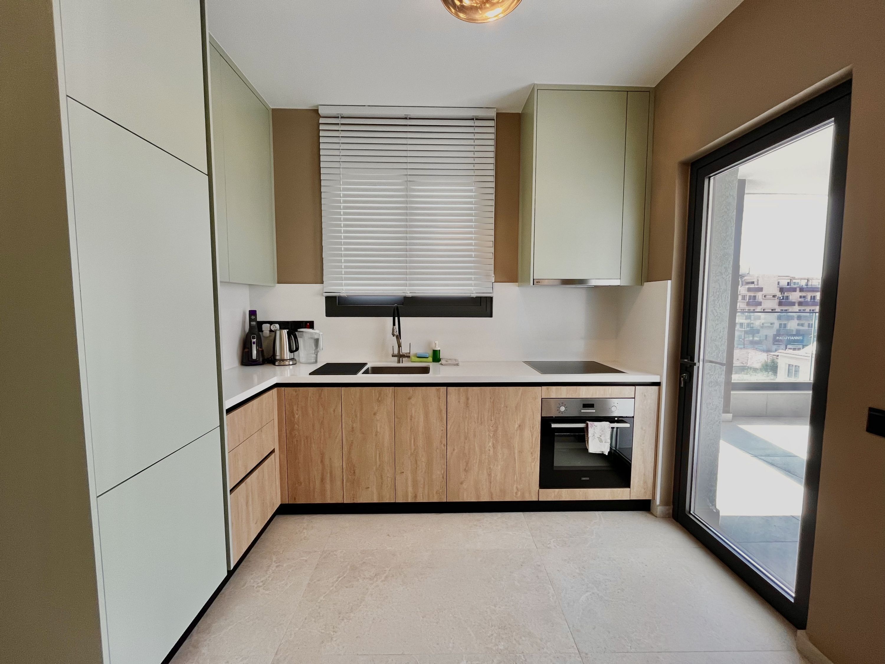 A compact kitchen with a built-in oven, a sink, and a window with blinds.
