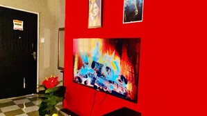 A room with a red wall, a television mounted on it, a wooden bench, and a door in the background.
