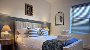 A neatly made bed with striped pillows, a bedside lamp, and a folded towel stack.