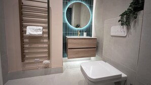 A modern bathroom with a towel rack, a wooden vanity, a white toilet, and a mirror with a circular frame.