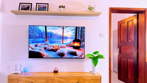 Un saló amb un gran televisor de pantalla plana a la paret, una taula de console de fusta i una planta en test.