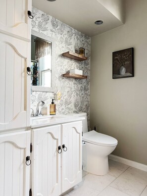 A bathroom with a white vanity, a toilet, a mirror, and a floral wallpaper.