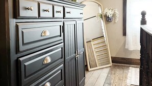 Une commode en bois foncé, dotée de nombreux tiroirs et de poignées, est placée dans une pièce dont le sol est en bois et le plafond est blanc.