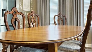 Une salle à manger avec une table et des chaises en bois, un papier peint à motifs et une grande fenêtre avec des rideaux.