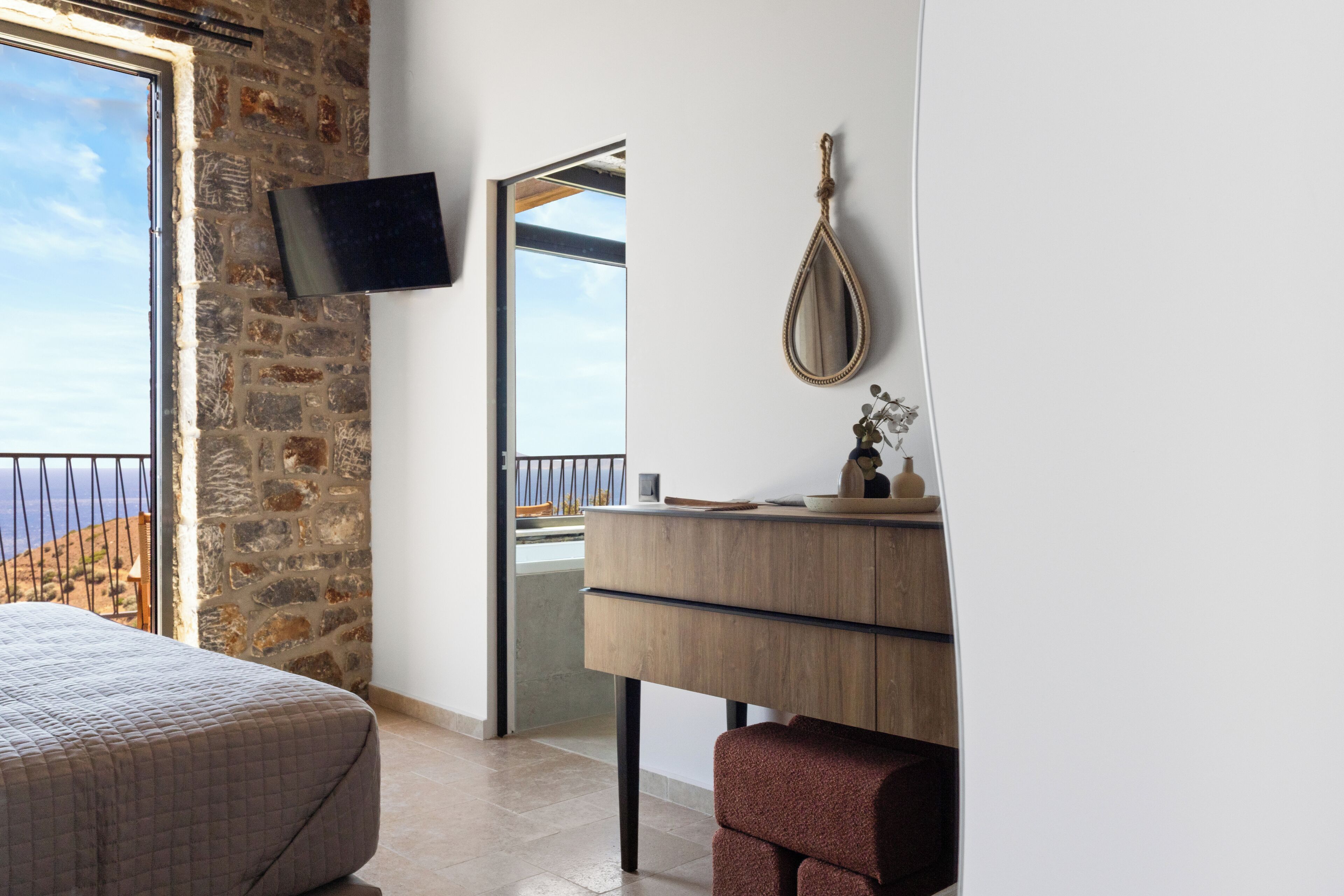 Ein Schlafzimmer mit Steingemäuer, einem Bett, einer Holzkommode, einem Spiegel und einem an der Wand montierten Fernseher.