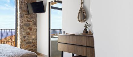 Ein Schlafzimmer mit Steingemäuer, einem Bett, einer Holzkommode, einem Spiegel und einem an der Wand montierten Fernseher.