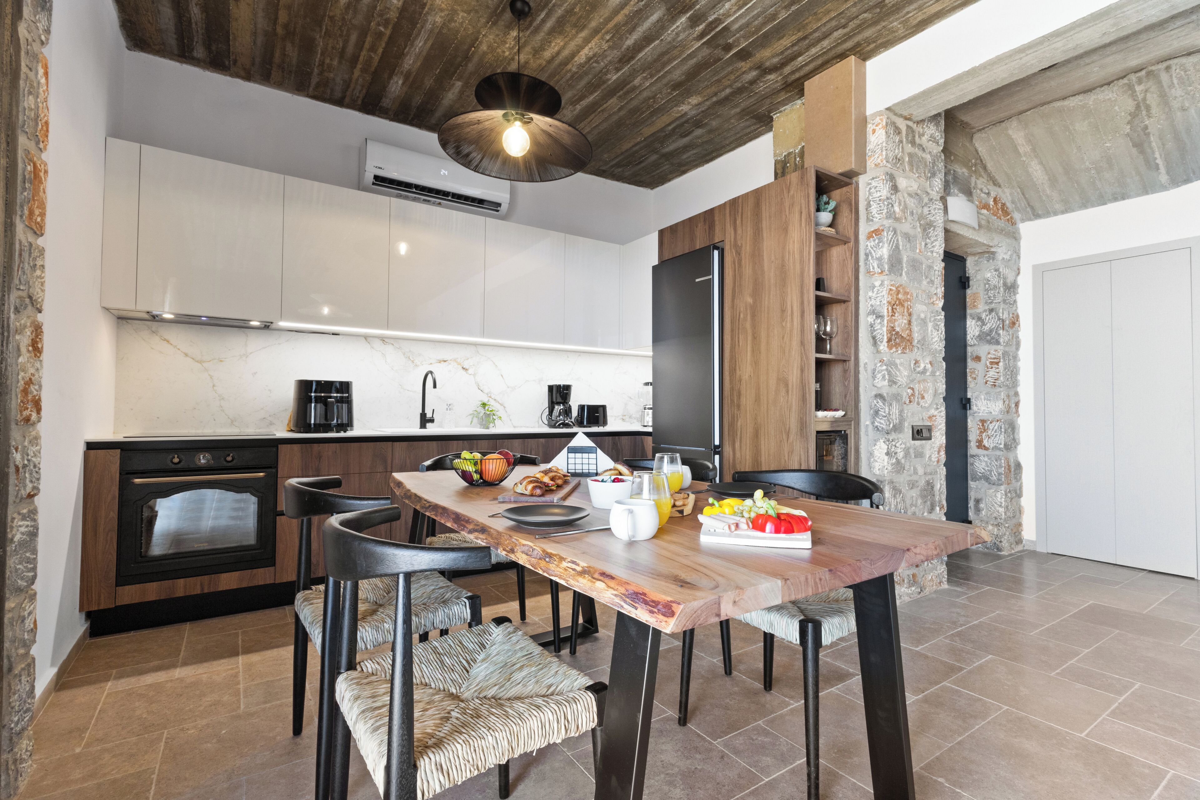A modern kitchen with a wooden dining table, built-in appliances, and a stone accent wall.