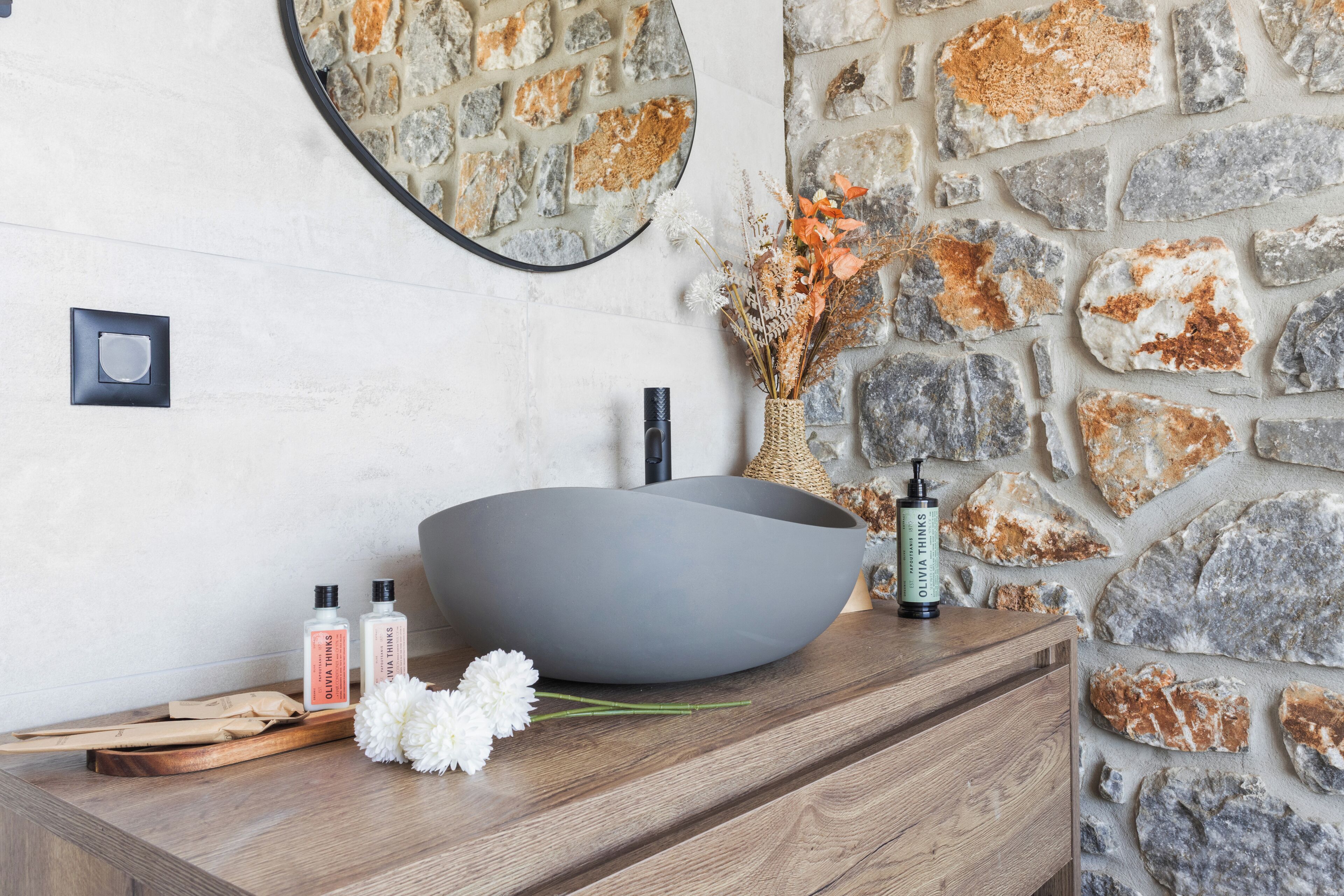 A bathroom vanity with a large, round, gray basin, a mirror, and toiletries.