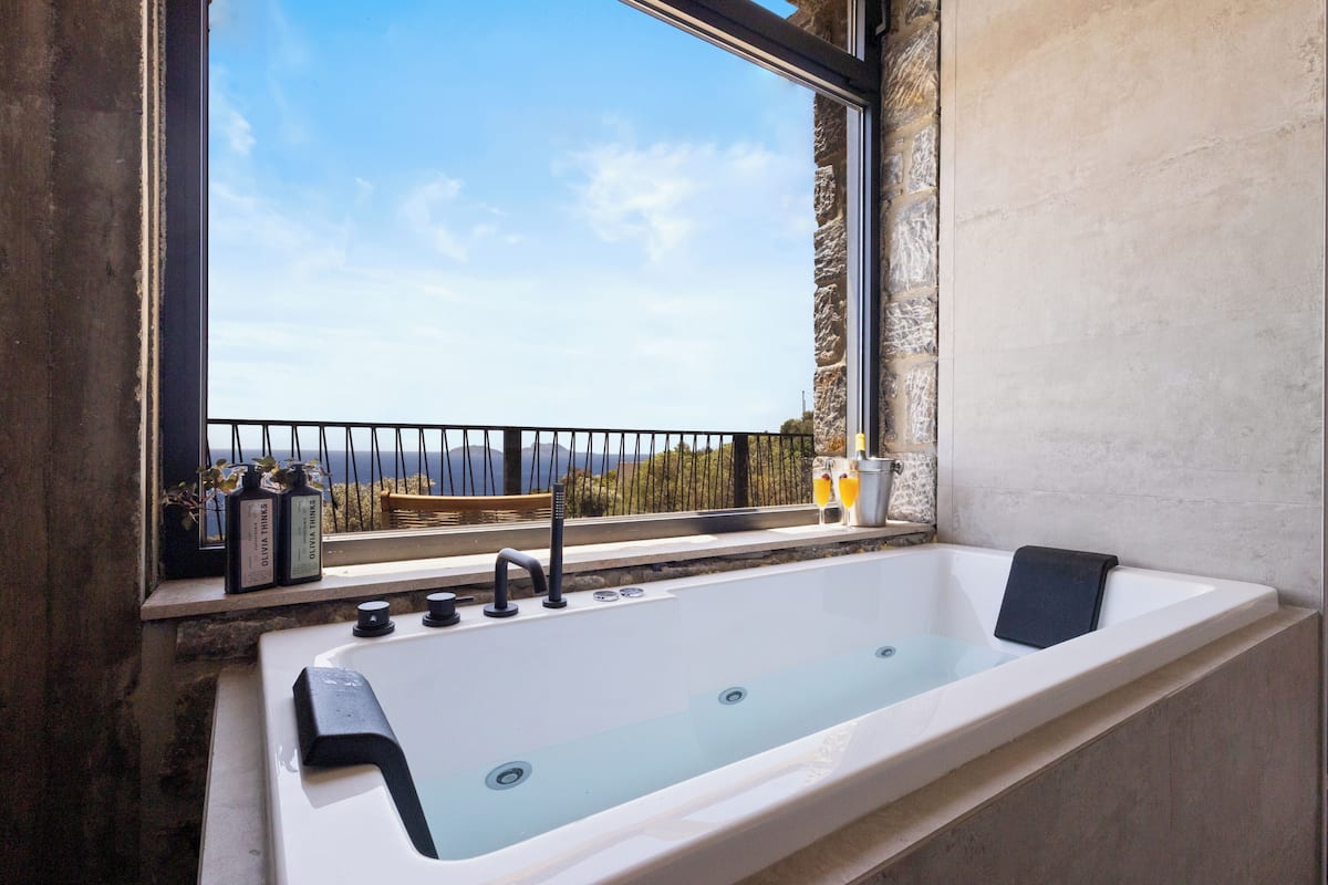 A large bathtub with a view of the sea through a window.