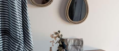 A wooden vanity with a mirror, a hat, a vase with dried flowers, a small bag, and a remote control.