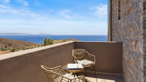 Un balcon avec deux fauteuils en osier et une petite table ronde, offrant une vue panoramique sur la mer et les collines.