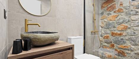 A bathroom with a stone sink, a wooden vanity, a toilet, and a shower with a stone wall.