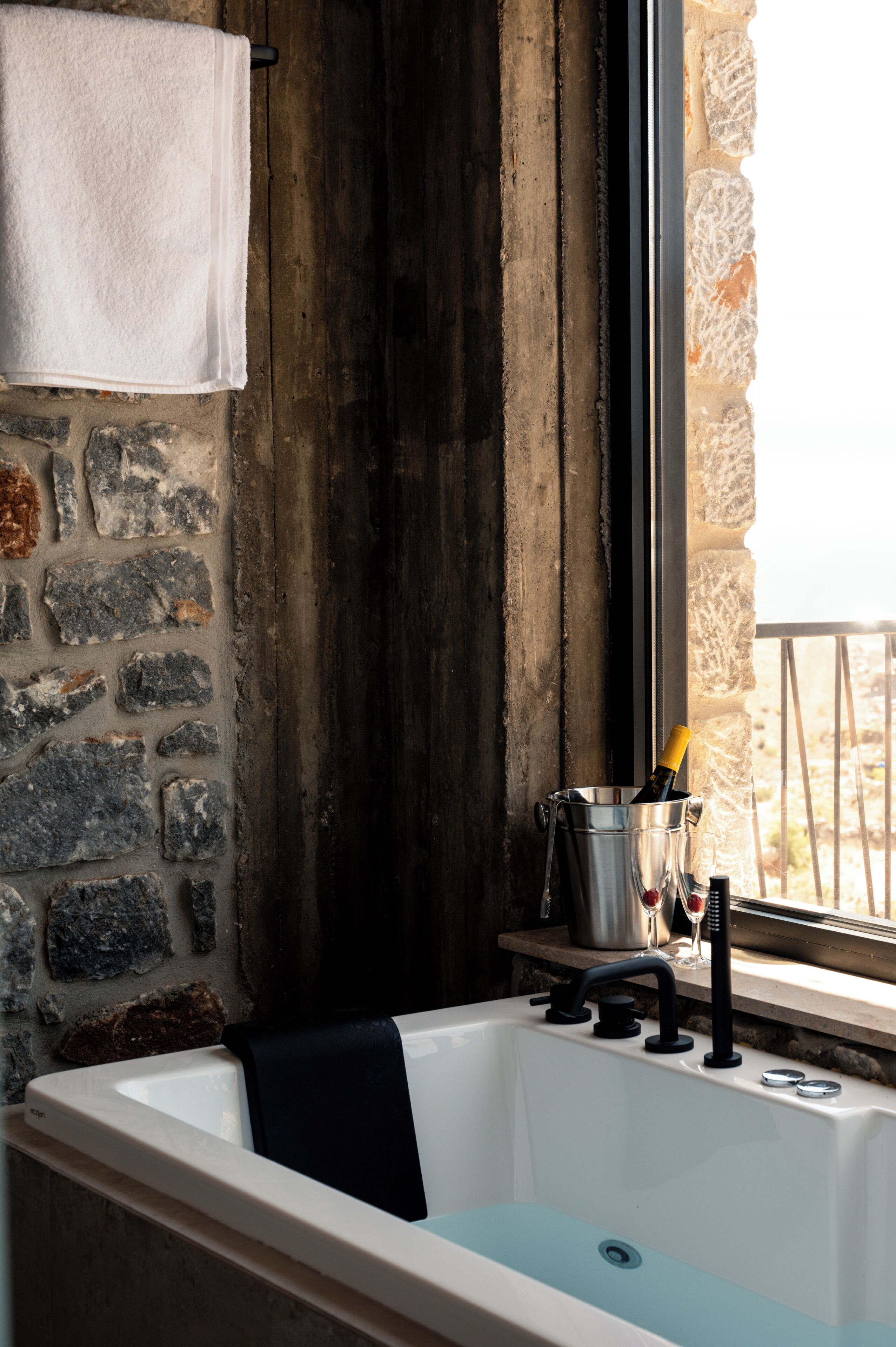A bathroom with a bathtub, a towel hanging on a rack, a wine glass, and a bottle in a bucket.