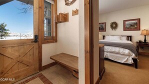 Une pièce avec une porte en bois, un banc, un lit et une vue sur un paysage enneigé.