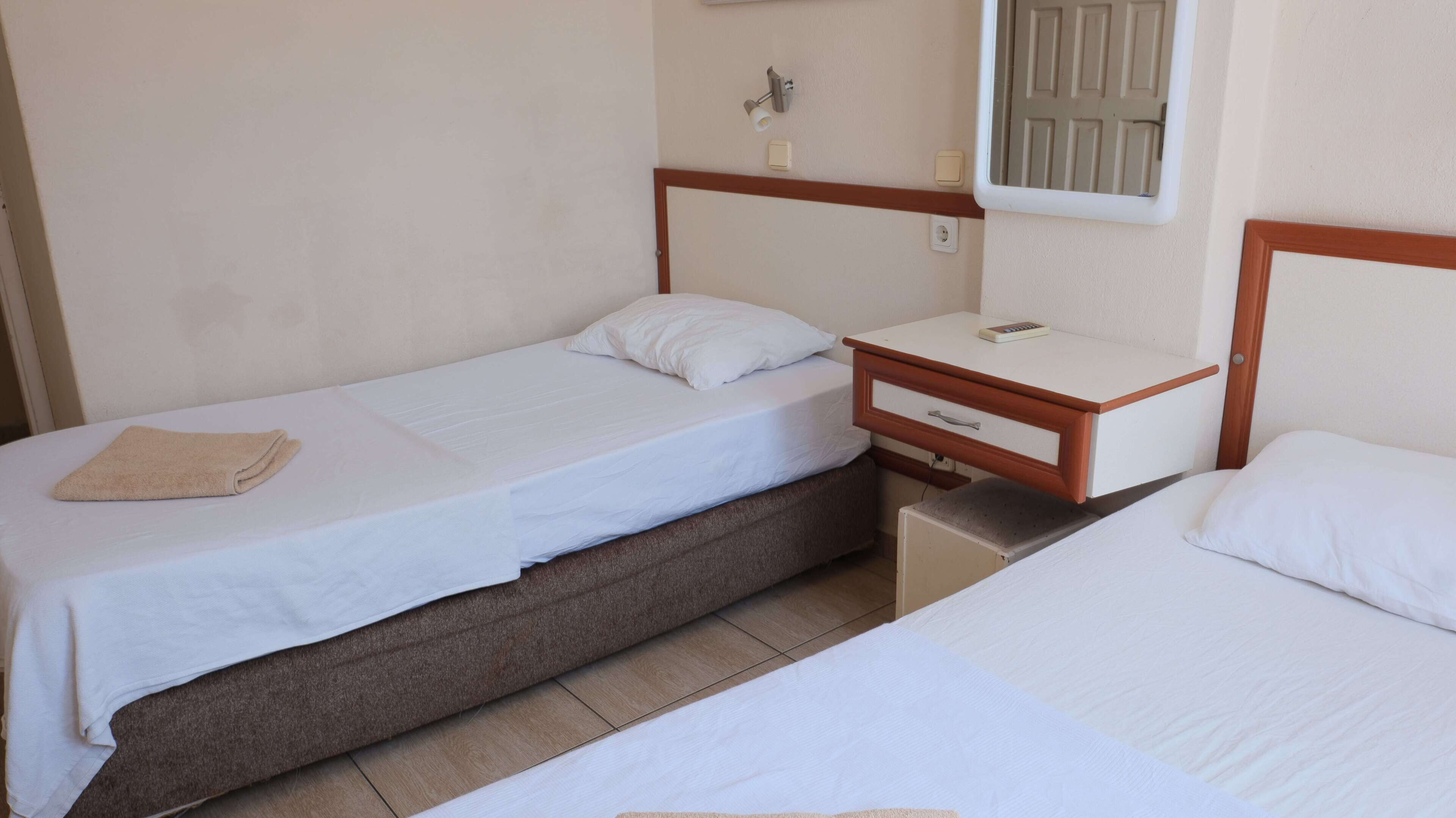 Une petite chambre propre, avec deux lits simples, une table de chevet en bois avec une lampe et un petit radiateur.