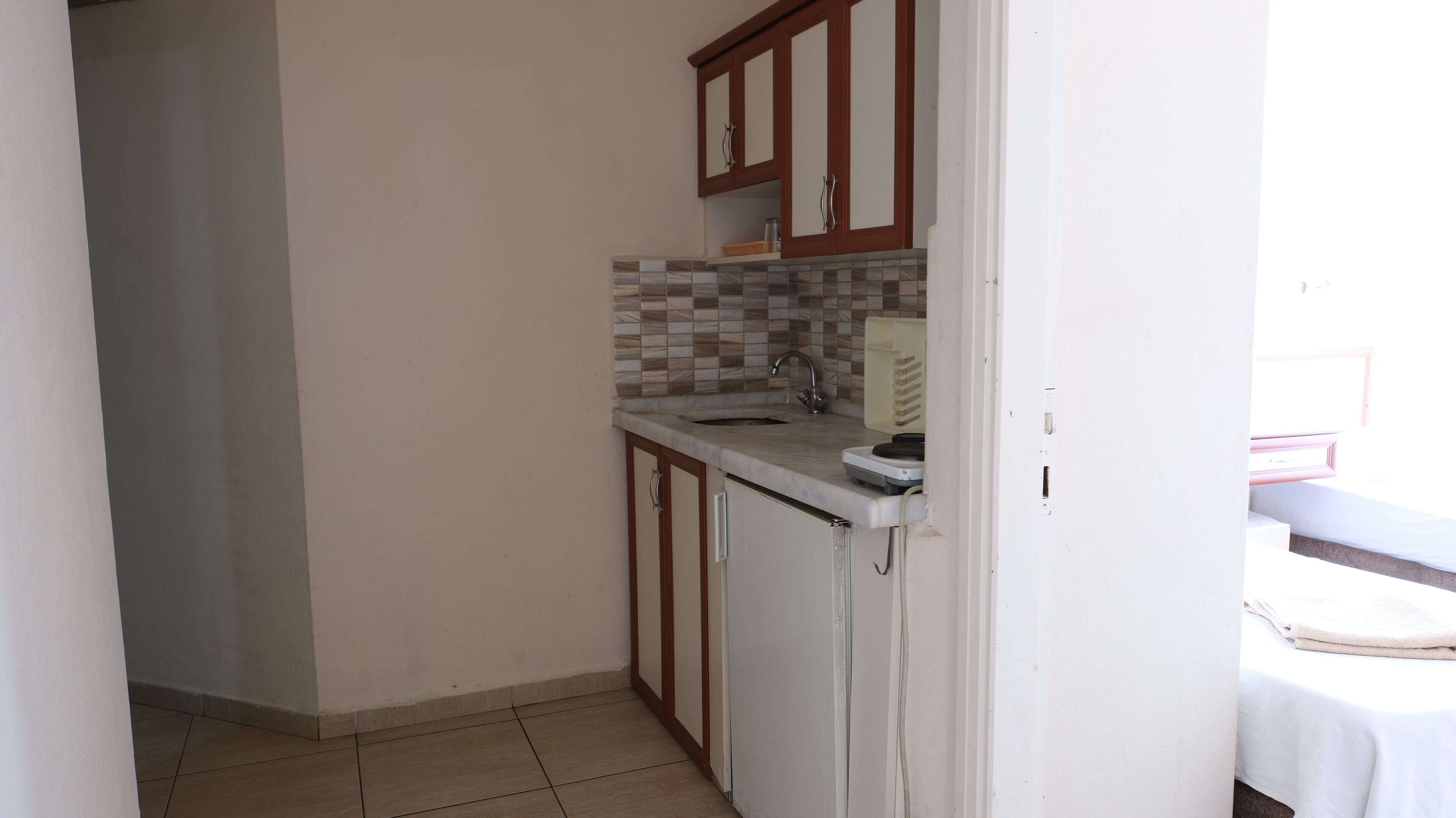 A small kitchenette with a tiled backsplash, a sink, and wooden cabinets.
