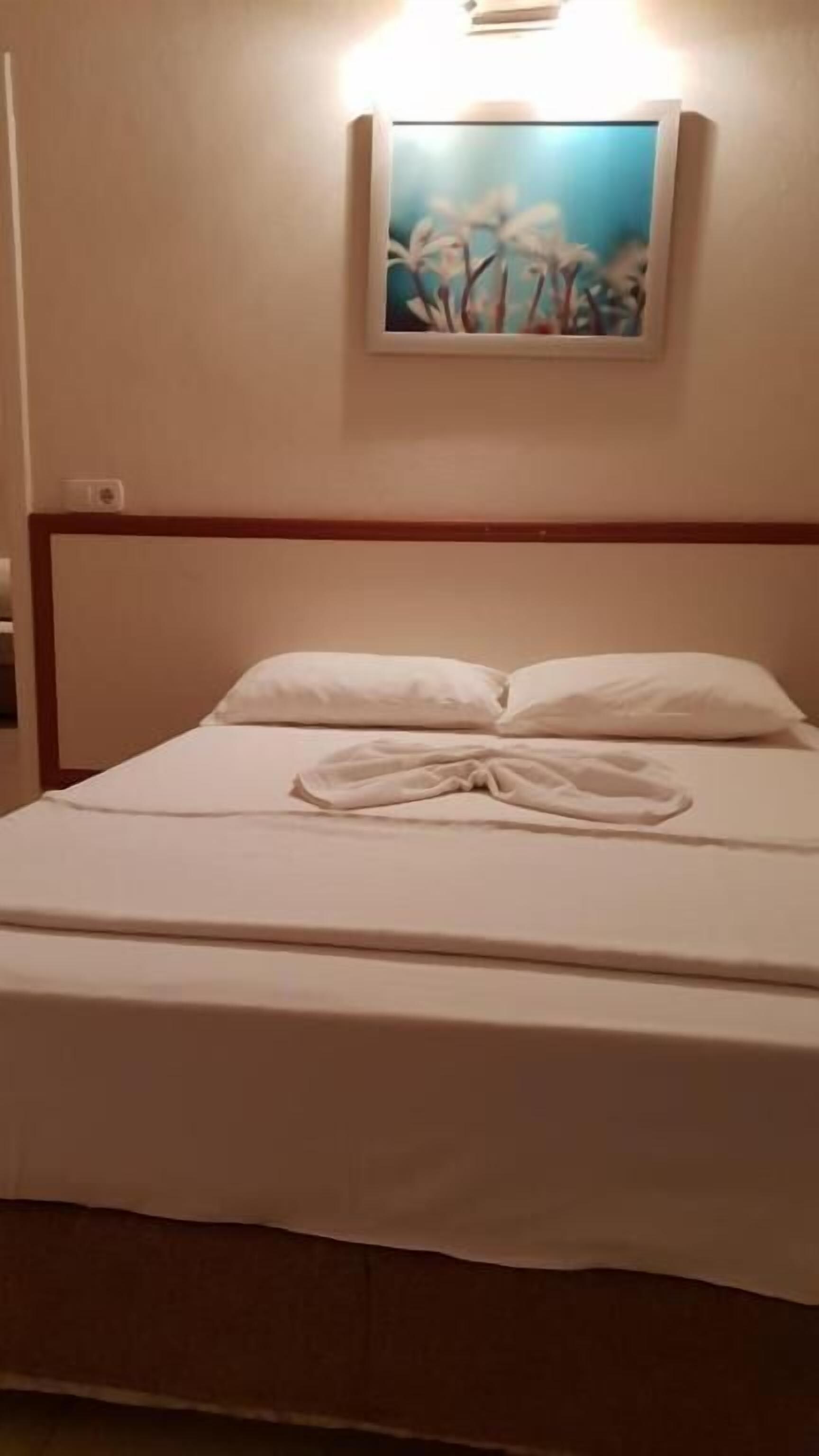 A neatly made bed with white linens and pillows, a painting of flowers on the wall above, and a wooden headboard.