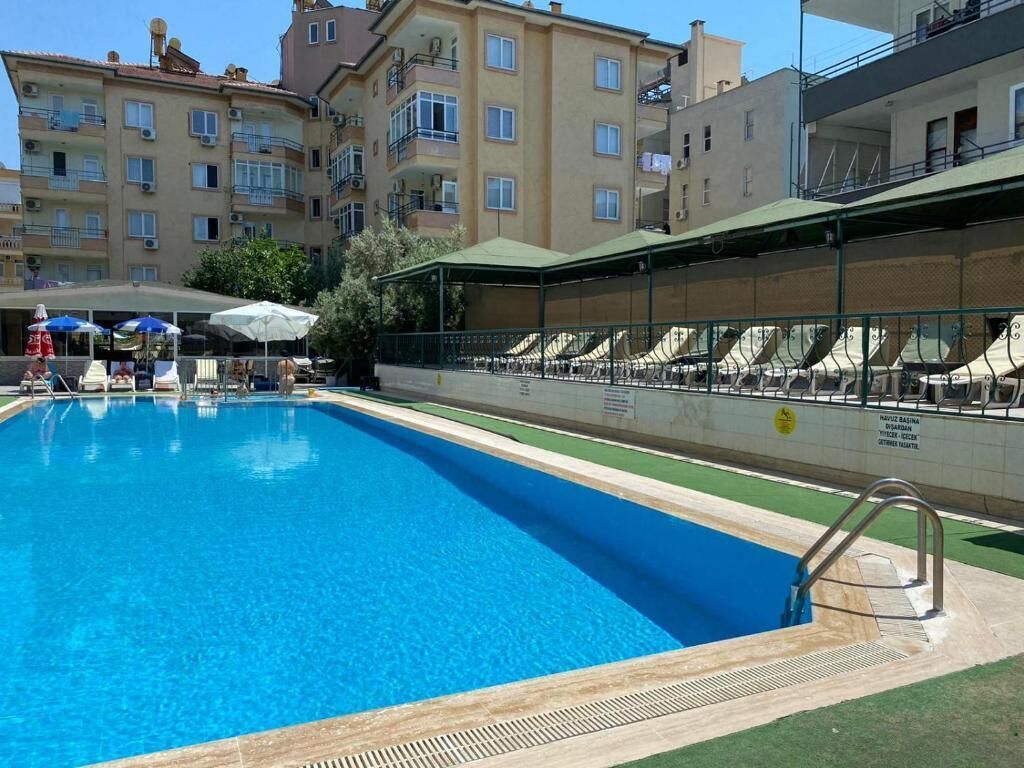 Una piscina con sillones de descanso y sombrillas, rodeada de edificios de varios pisos.
