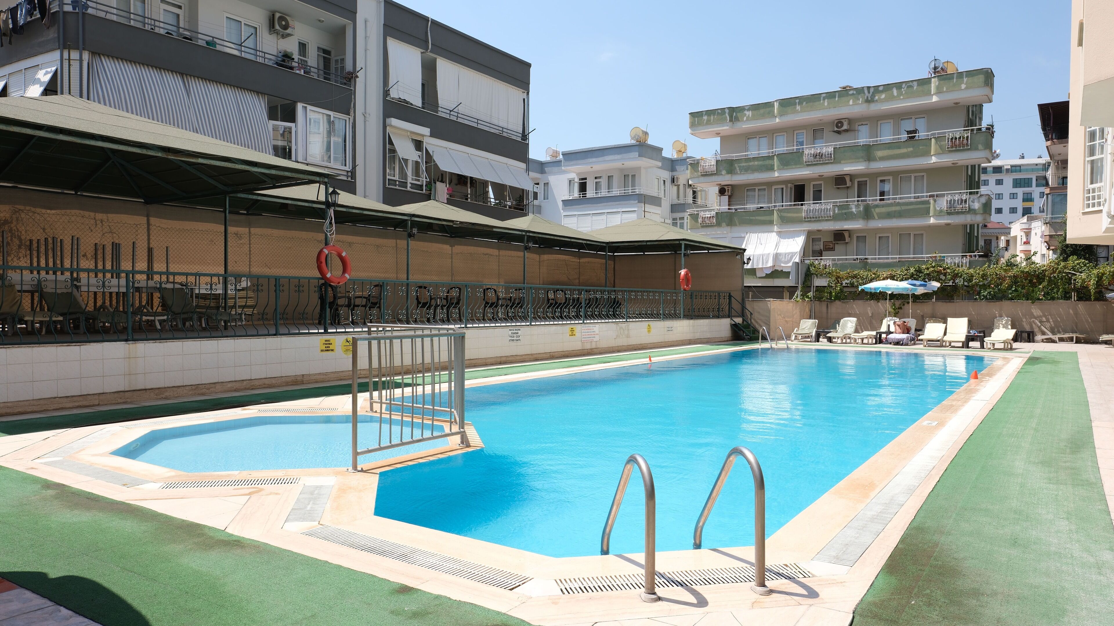 Una piscina con tabla de clavados, rodeada de sillas de descanso y una zona de estar cubierta.