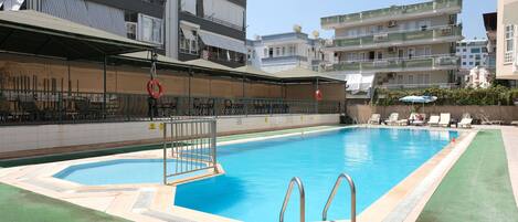 Una piscina con tabla de clavados, rodeada de sillas de descanso y una zona de estar cubierta.