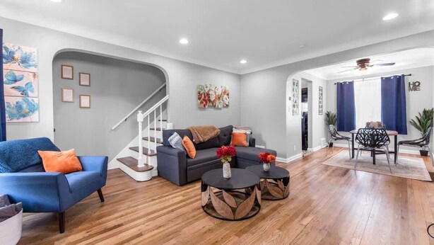 A modern living room with a grey sofa, blue armchair, and two round coffee tables with leaf-patterned bases. A staircase with a white railing leads to a second floor. - Brooklyn Townhome| Updated Kitchen| Sleeps 9 (Brooklyn)
