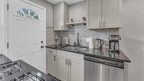 A modern kitchen with white cabinets, a stainless steel dishwasher, and a black countertop. - Brooklyn Townhome| Updated Kitchen| Sleeps 9 (Brooklyn)