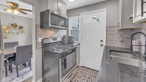 A modern kitchen with stainless steel appliances, a dining area with a gray table and chairs, and a patterned rug. - Brooklyn Townhome| Updated Kitchen| Sleeps 9 (Brooklyn)