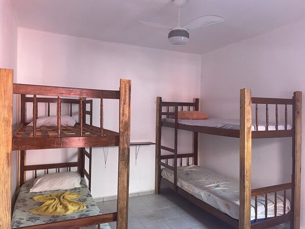A room with three bunk beds, a ceiling fan, and a plain white wall.