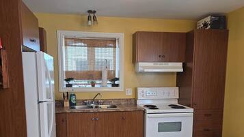 Una cocina compacta con armarios de madera, un refrigerador blanco, una estufa y una ventana con persianas.