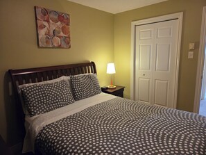 Ein Schlafzimmer mit Bett, Nachttisch, Lampe, Tür und einem Wandbild.