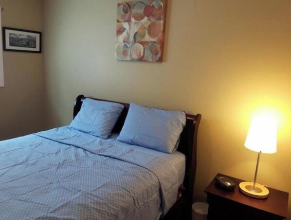 Ein ordentlich bezogenes Bett mit einer blauen und weißen Bettdecke, einem Holzkopfschild und einem an der Wand befestigten abstrakten Kunstwerk darüber.