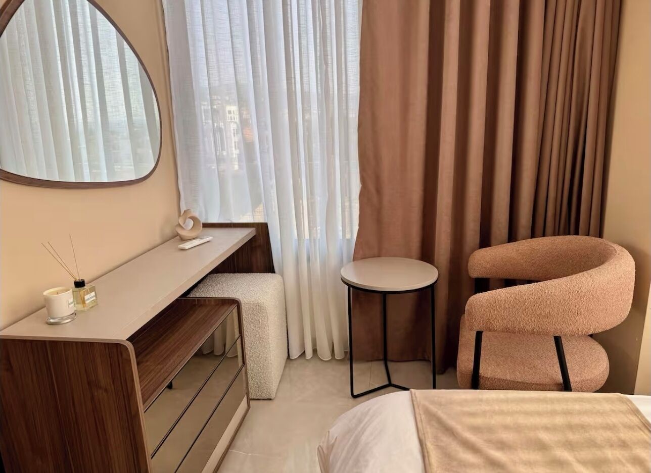 A hotel room with a wooden desk, a round table, a curved armchair, and a bed.
