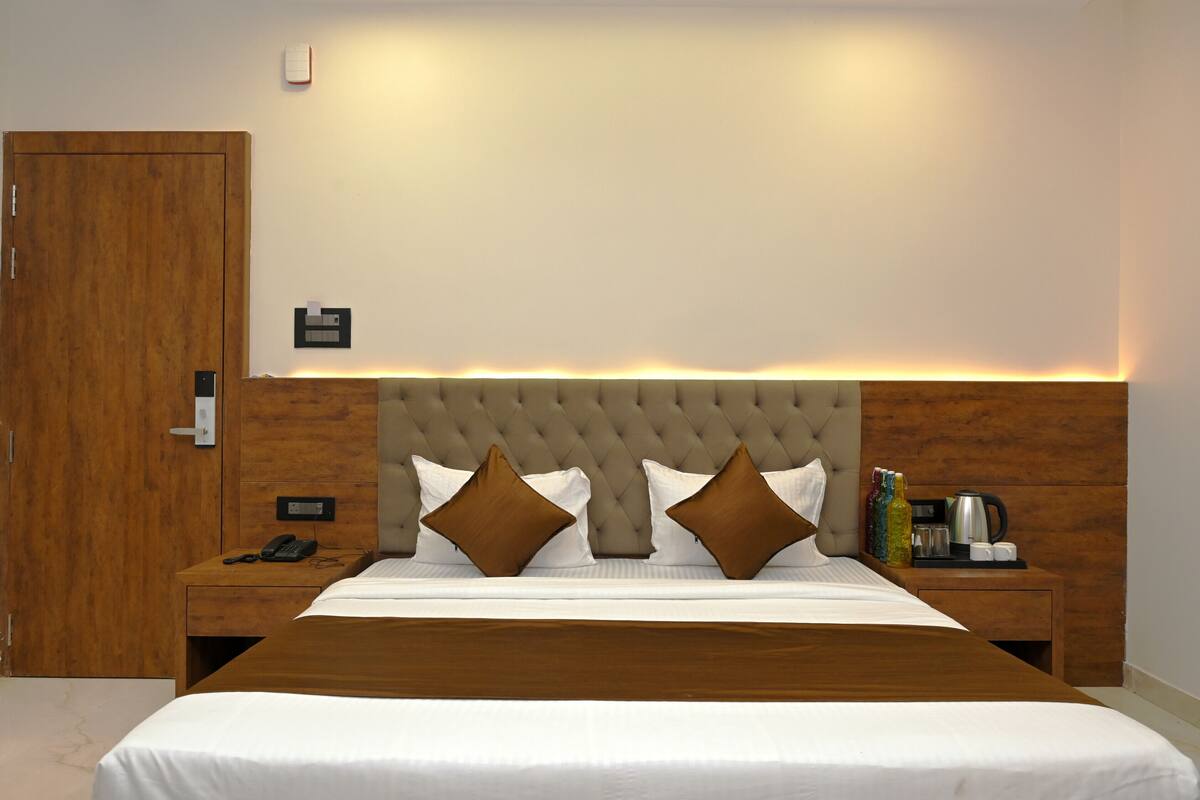 A hotel room with a large bed, wooden headboard, two bedside tables with a phone and a kettle, and a wooden wardrobe.