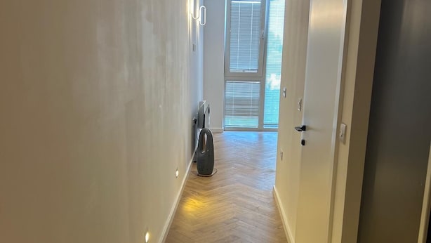 Un pasillo con piso de madera, paredes blancas y una puerta que da a un balcón con vistas.