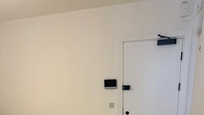Un dormitorio con cama, una puerta blanca y un pequeño panel de control en la pared.