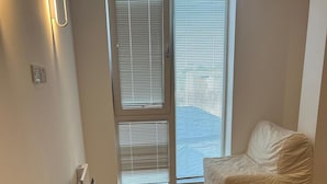 Una habitación con piso de espiga, un sofá blanco y una puerta de vidrio corredera con persianas.