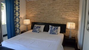 A hotel room with a stone-patterned wall, a bed with white bedding, two decorative pillows, and two bedside lamps. - Cabarete Center, 1BR Apartment with Sea View (Cabarete)