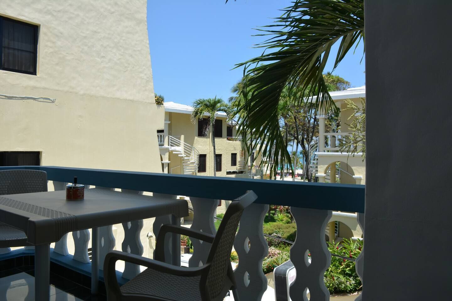 A balcony with a table and chairs, overlooking a building with multiple balconies and palm trees.