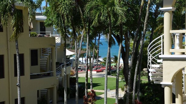 A resort with a pool area, palm trees, and a view of the ocean. - Cabarete Center, 1BR Apartment with Sea View (Cabarete)