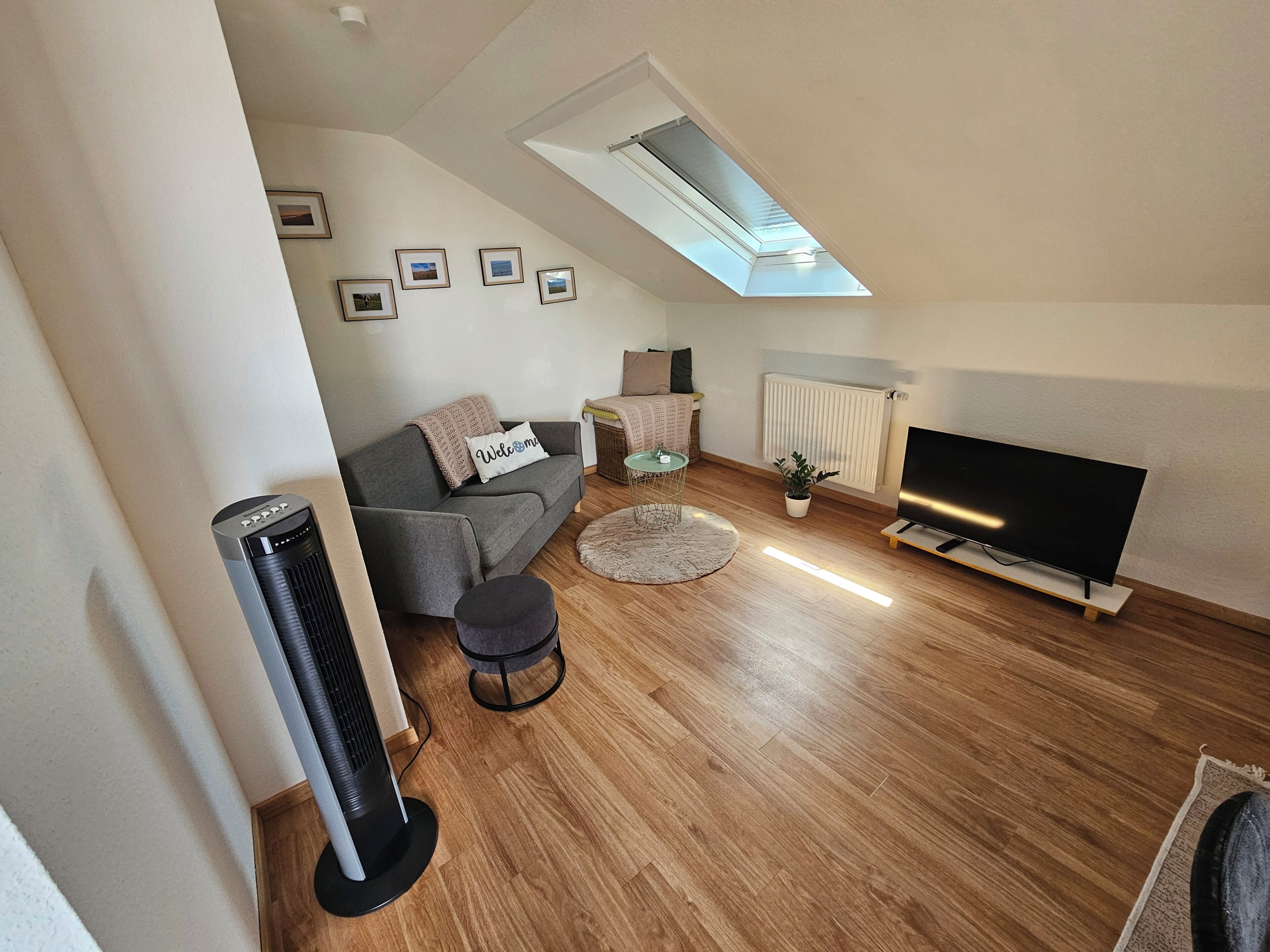 Ein modernes Wohnzimmer mit grauem Sofa, pouf, Standheizung, Flachbildfernseher und Oberlicht.