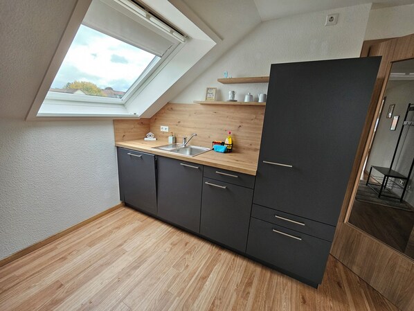 A compact kitchen with a skylight, dark cabinets, and a wooden countertop.