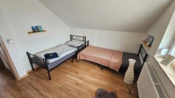 Una habitación pequeña con cama individual, techo inclinado, un radiador y una estantería con libros.