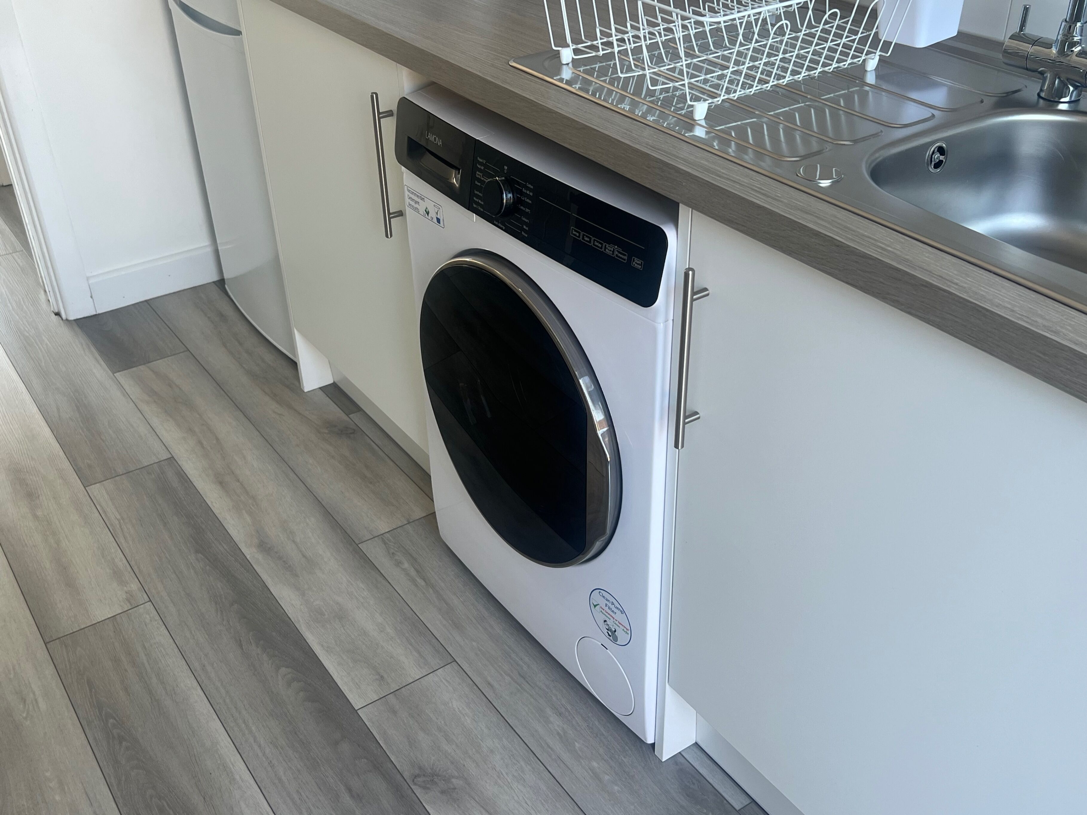 Una cocina moderna con lavadora integrada, un lavamanos de acero inoxidable y encimera de madera.