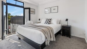 A modern bedroom with a large bed, a nightstand, and a view through a sliding door to the outside.