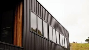 En modern byggnad med en mörk fasad, stora fönster och en tydligt synlig trädörr.